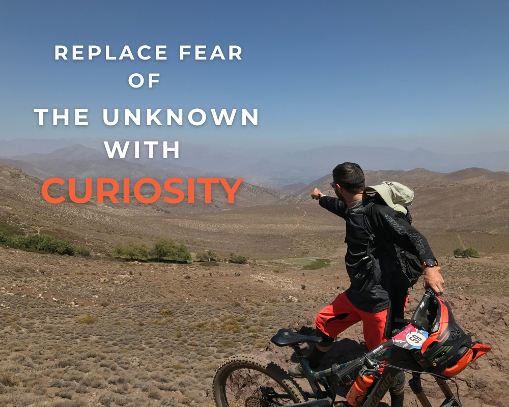 Richard Duke, mountain biking in the Andes, pointing into the distance with text overlay: “Replace Fear of the Unknown with Curiosity” – symbolising bold career decisions and embracing new challenges.