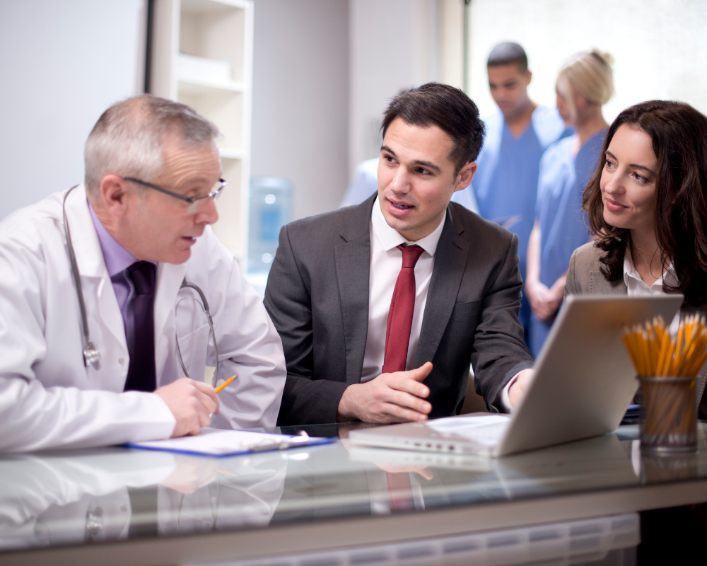 Medical sales professionals discussing product strategies with a doctor in a clinical setting, highlighting expertise and collaboration.
