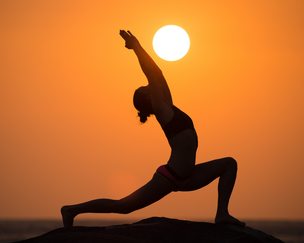 Person doing yoga against the sun silhouette
