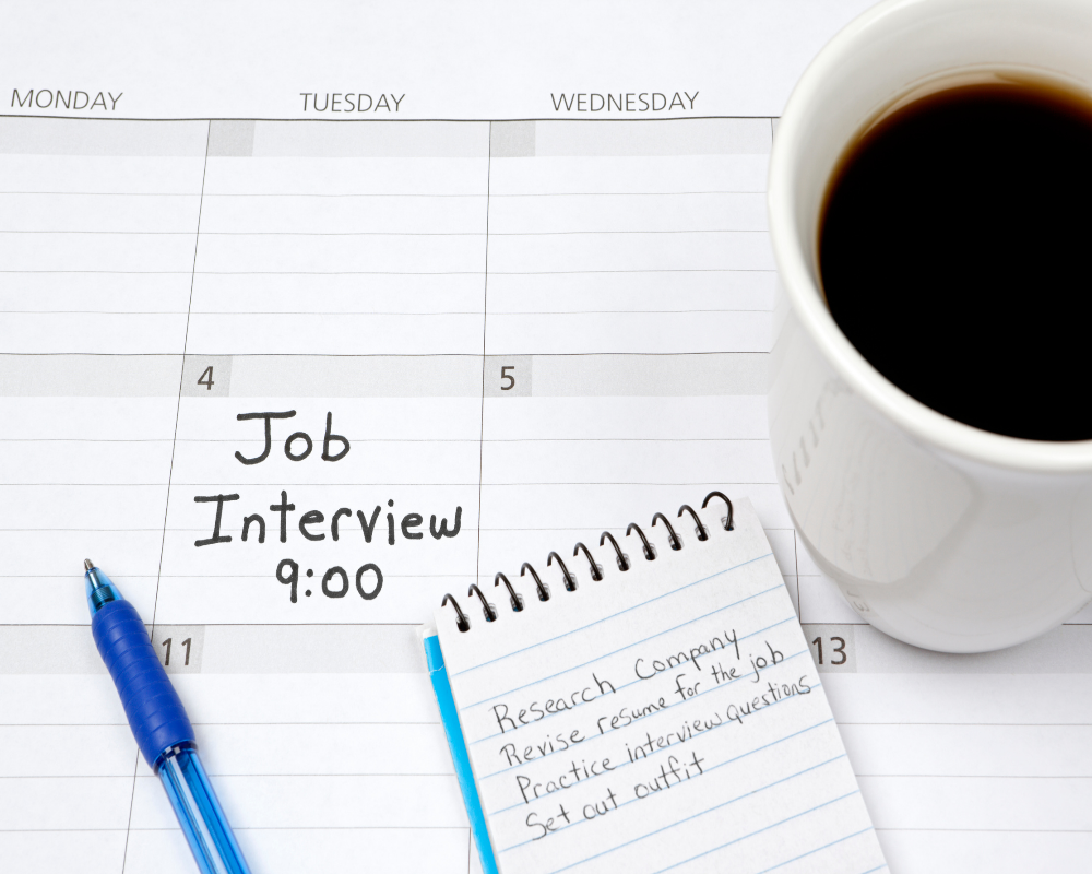 A calendar marked with ‘Job Interview 9:00 AM,’ a notepad with preparation notes, and a cup of coffee.