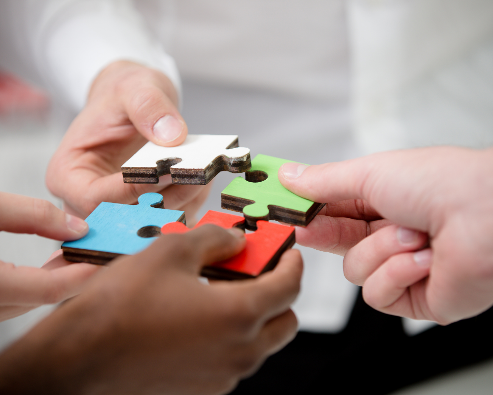 People's hands holding pieces of puzzles bring them together.