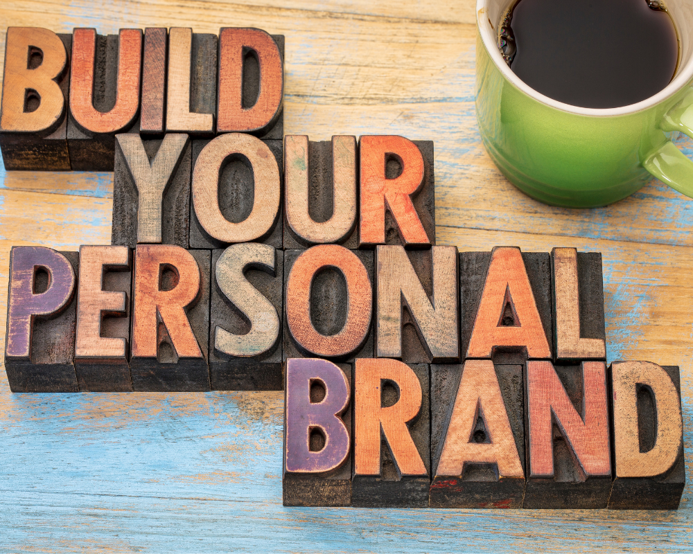 Wooden letters spelling ‘Build Your Personal Brand’ on a desk with a coffee cup, representing career growth and professional branding