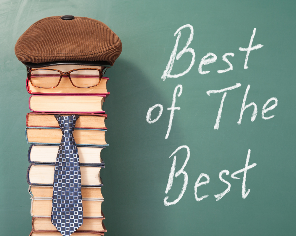 Pile of books with hat, tie, and glasses against a chalkboard with words best of the best.