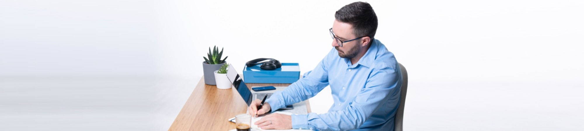 Man at desk writing a blog making notes with a pen